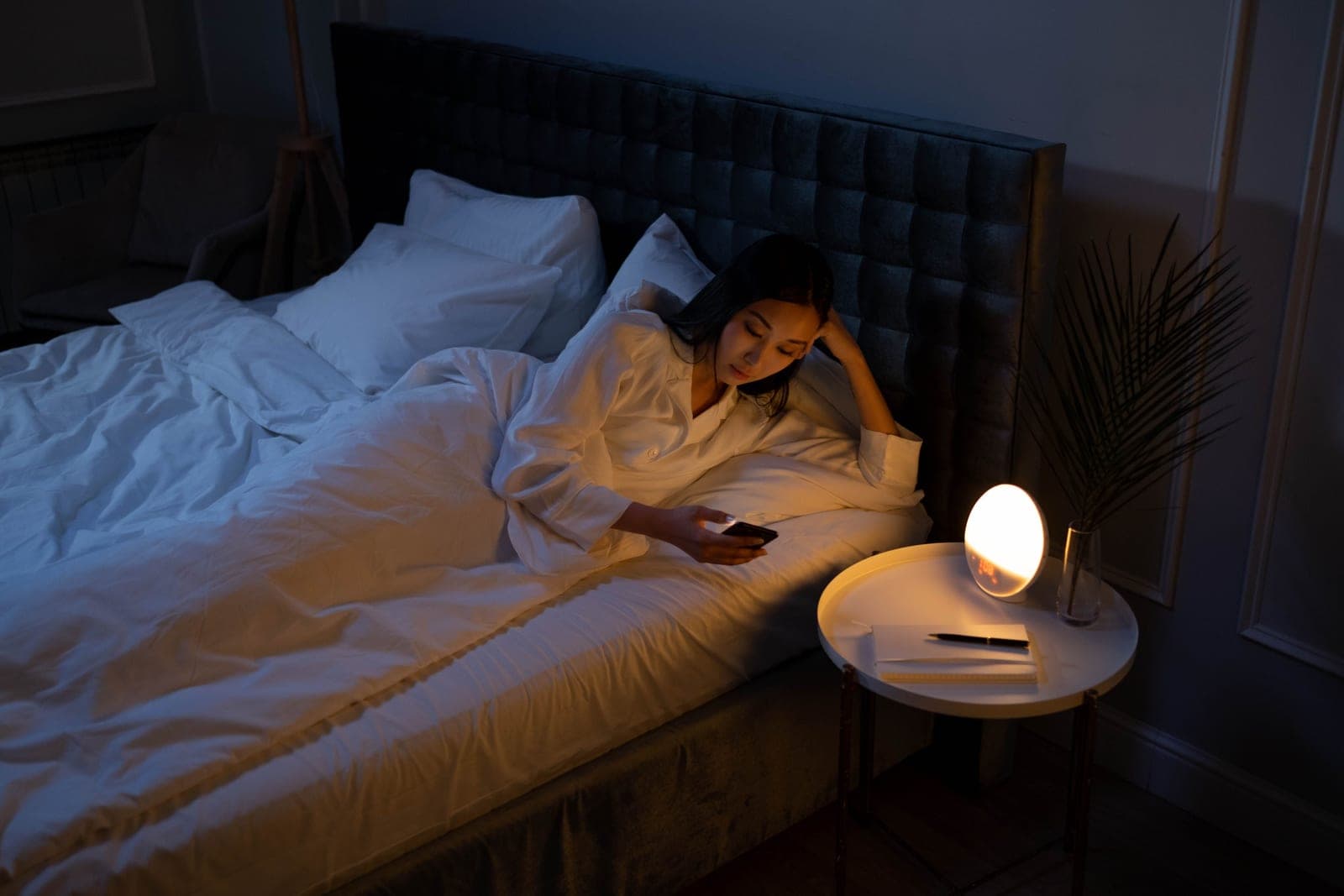 A person in bed using a phone beside a glowing bedside lamp