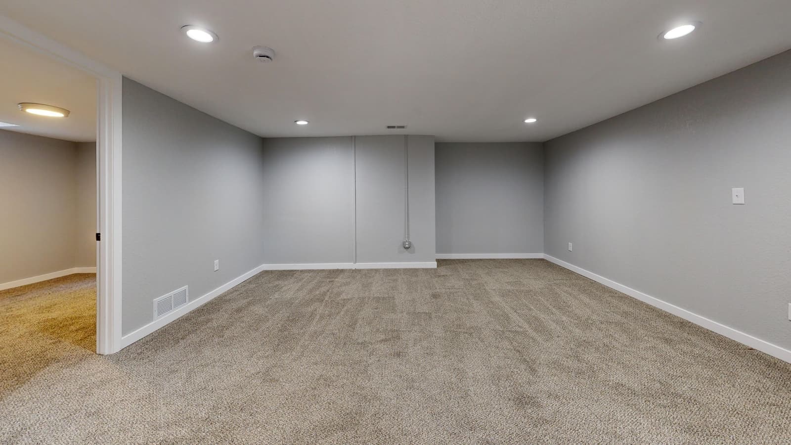 A finished basement room lit by linear ceiling fixtures