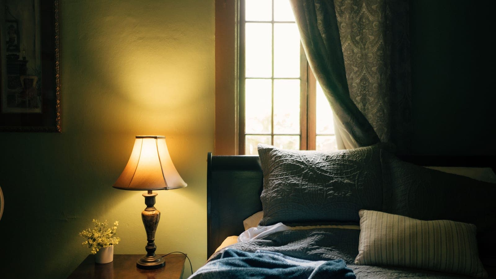 A small lamp lit on a bedside table beside a book