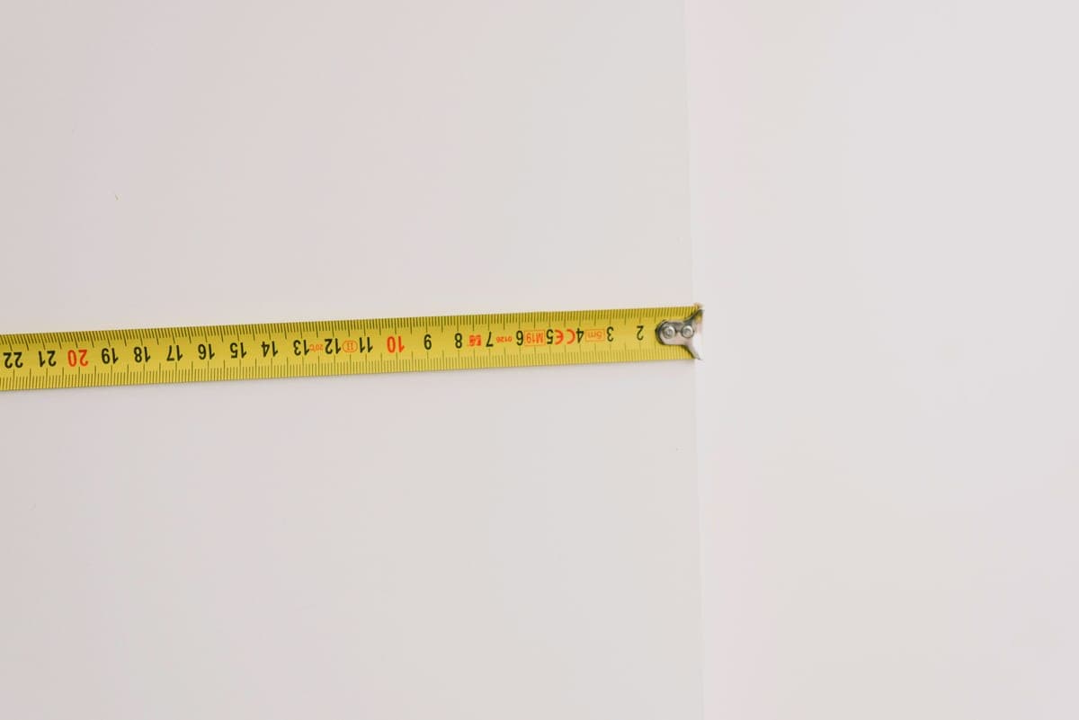 A tape measure and notepad on a table beside a lit lamp, used to size a room