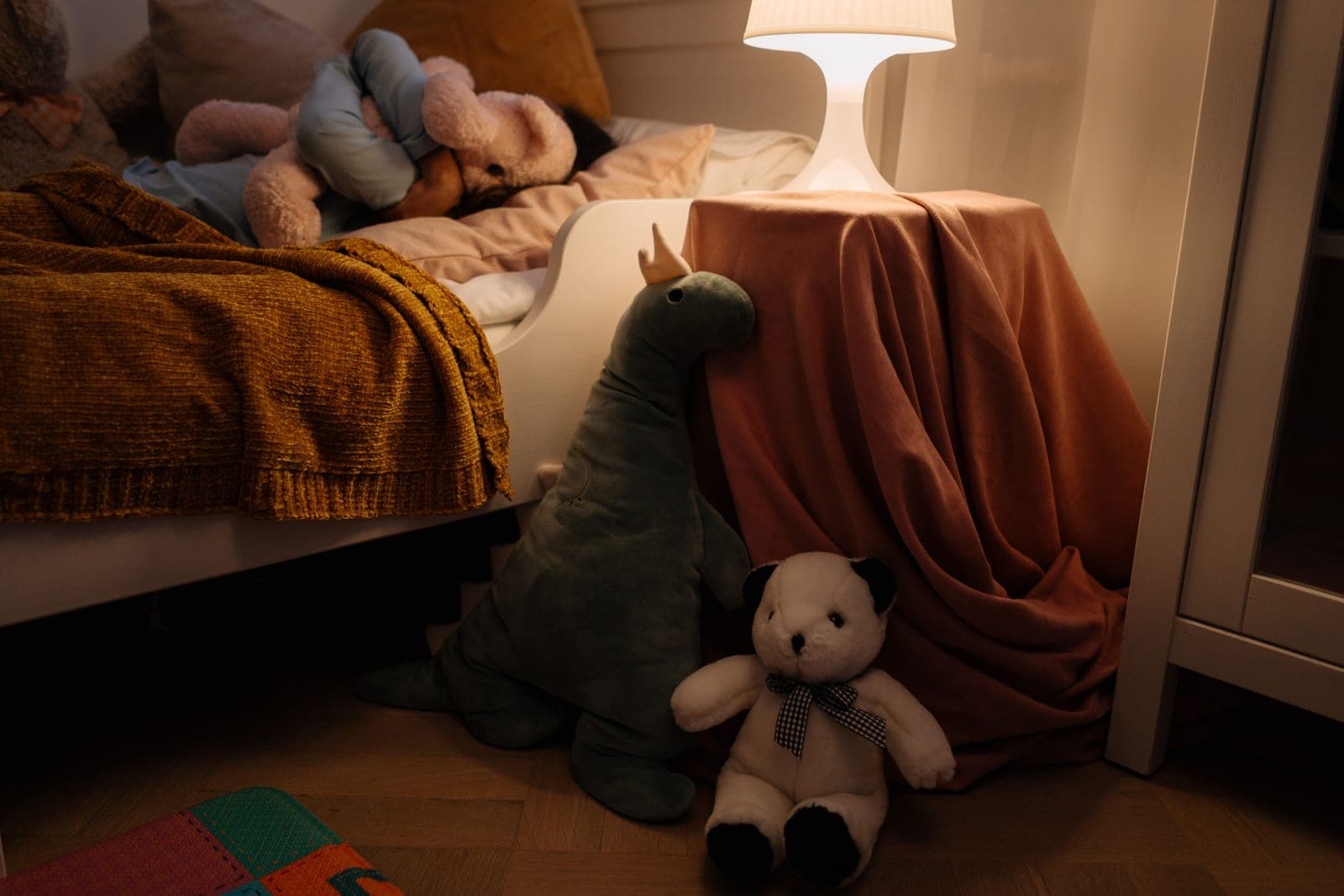 A child's bedroom lit warmly by a bedside lamp in the evening