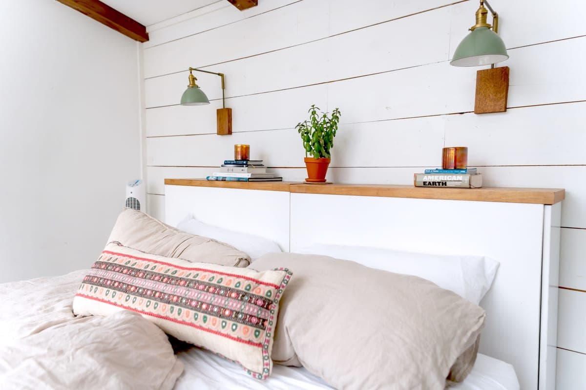 A wall sconce mounted beside a bed with its cord running down to an outlet