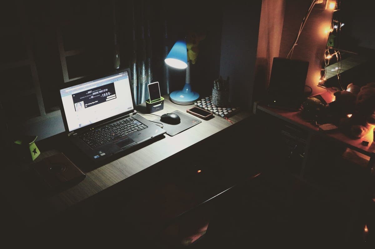 A home office desk lit by a task lamp beside a monitor