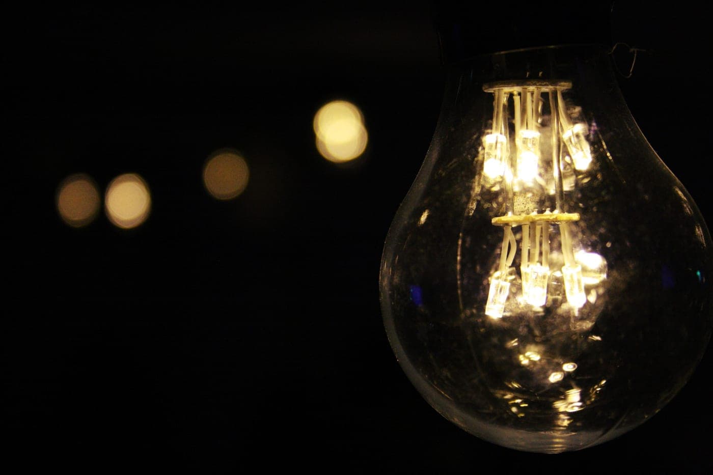 A warm-toned LED bulb glowing in a bare pendant socket against a plain wall