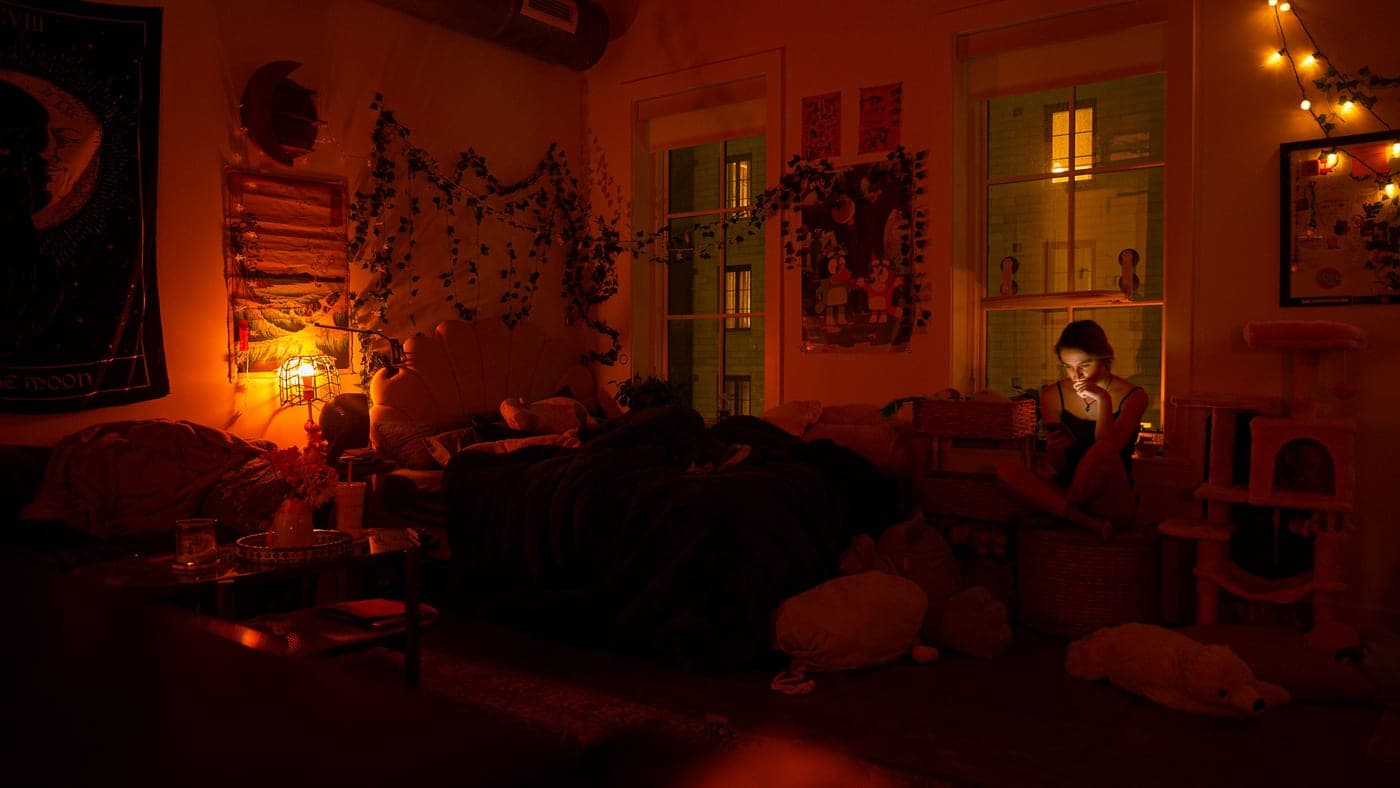 A phone on a table beside a lamp glowing warm in a dim apartment living room at night